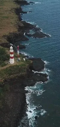 This phone live wallpaper depicts a lighthouse on a rocky cliff by the ocean, set against a backdrop of Romain Brook