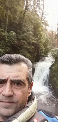 This lively wallpaper showcases a breathtaking waterfall that serves as the backdrop to a man taking a selfie portrait