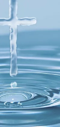 This stunning live phone wallpaper features a cross in the center of a body of serene water, with drops of fresh water falling from the top of the screen