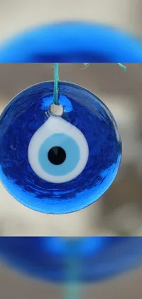 This phone live wallpaper features a vibrant blue evil eye ornament, hung on a string against a subtle blue background