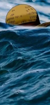 This live wallpaper features a photorealistic painting by David Rubín of a yellow hat on dangerous waves in a body of water