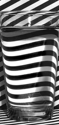 This phone live wallpaper boasts a captivating black and white photo of a glass of water on a striped surface, incorporating op art and dazzle camouflage elements for a hypnotizing effect