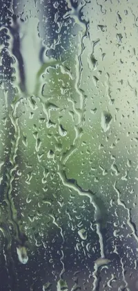 This live wallpaper features a close up of a rainy window with greenish liquid raindrops running down the glass