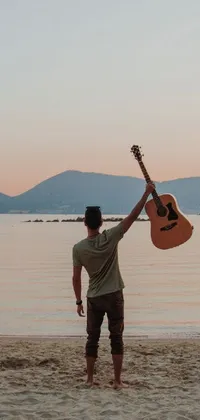 This phone live wallpaper features a peaceful scene of a man standing on a beach with a guitar