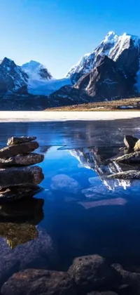 This stunning phone live wallpaper features a pile of rocks sitting on top of a crystal clear lake, set against a breathtaking Himalayan landscape with snow-capped mountains in the distance