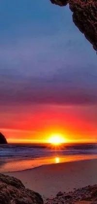 This phone live wallpaper showcases a stunning sunset over a beach cave