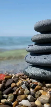 This phone live wallpaper showcases a mesmerizing artwork with a pile of rocks sitting atop a beach beside the ocean