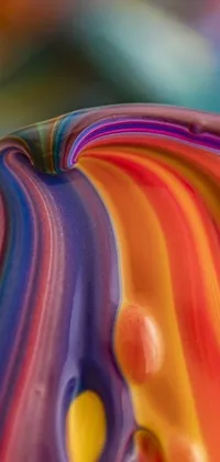 This phone live wallpaper showcases a stunning close-up of a colorful blown glass object, resting on a table