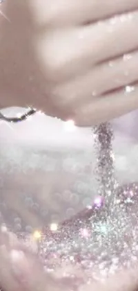 This phone live wallpaper features a close-up of a hand holding a cell phone, surrounded by sparkling diamonds and a heavenly pink color scheme