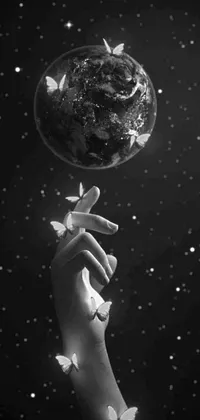 This black and white live wallpaper features a surrealistic photo of a hand holding a globe, surrounded by stars and flowers