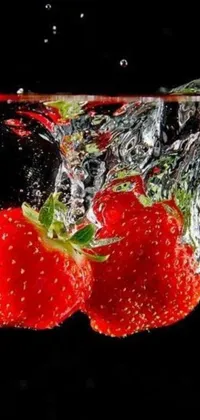 This live phone wallpaper features a mesmerizing image of two realistic strawberries falling into a body of water