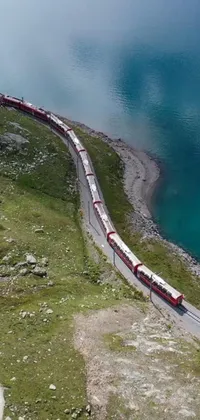 Transform your phone screen with a stunning live wallpaper of a long train on a steel track next to a peaceful body of water, set against the mesmerizing backdrop of the Swiss Alps