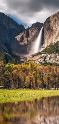 This phone live wallpaper showcases a gorgeous scene of a serene body of water with a captivating waterfall in the background, set against the majestic backdrop of a mountain and a picturesque meadow with rich colors of fall