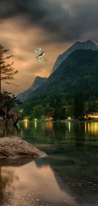 This phone live wallpaper features a colorful kite flying over a serene body of water surrounded by trees and mountains