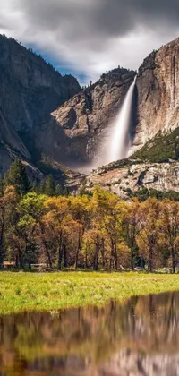 This phone live wallpaper depicts a picturesque body of water with a beautiful waterfall and a mountain range in the background, set in a serene meadow landscape