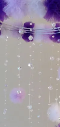 This phone live wallpaper boasts purple and white pom poms suspended from a ceiling with kinetic arts that sparkle with diamonds and crystals, set against a fluffy pastel purple background with arcs of light beams