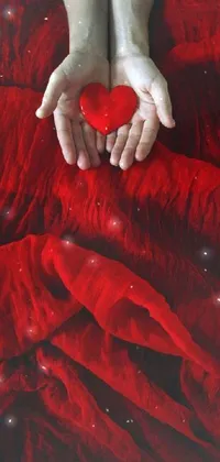 This phone wallpaper features a red heart cradled in someone's hands