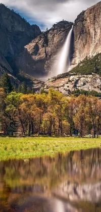 This phone live wallpaper showcases a beautiful waterbody consisting of a waterfall with a striking backdrop of mountains and a meadow in autumn colors