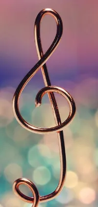 This live phone wallpaper features a stunning macro photograph of a colorful copper and brass musical note on a string