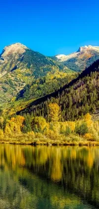 Looking for a calming and serene live wallpaper for your phone? Look no further than this beautiful image of a mountain range in Colorado, with vibrant and colorful trees and a shimmering body of water in the foreground