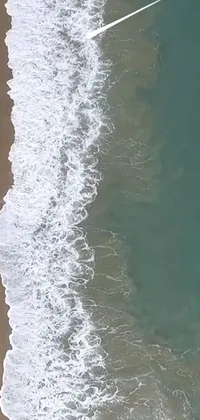 This visually stunning phone live wallpaper features an aerial shot of a surfer riding the waves on a sandy beach