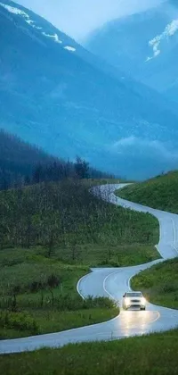 This phone live wallpaper features a car driving down a winding road amidst breathtaking natural scenery