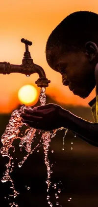 This stunning phone live wallpaper showcases a young boy quenching his thirst by drinking water from a faucet located in an African river