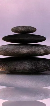 This live phone wallpaper showcases a minimalist and tranquil scene of a stack of rocks sitting on a reflective surface
