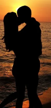 This phone live wallpaper showcases a beautiful and romantic scene of a couple kissing on the beach during sunset