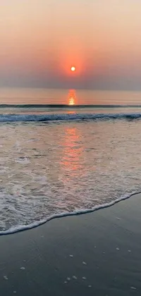This phone wallpaper showcases a picturesque sunset at the beach, with the sun setting over the tranquil waters