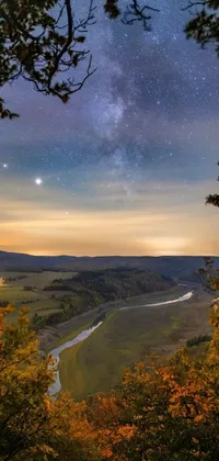 The phone live wallpaper showcases a stunning autumn night landscape of a river flowing through a verdant green valley, with a mesmerizing night sky backdrop