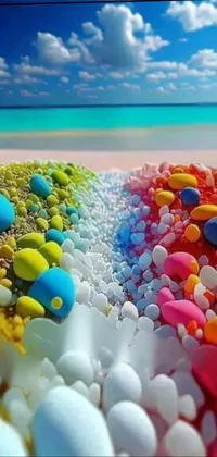 This lively phone live wallpaper features a photorealistic painting of colorful rocks on a sun-soaked beach, set against a backdrop of the sparkling blue ocean