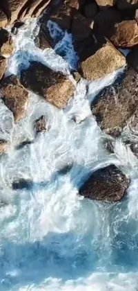 This phone live wallpaper showcases a beautiful bird's eye view of a peaceful body of water surrounded by rustic rocks
