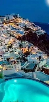 This phone live wallpaper showcases a serene cityscape of Santorini island at night with a stunning pool in the forefront