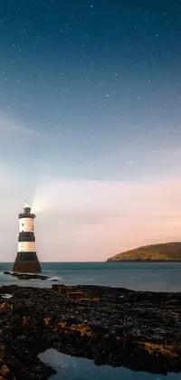 This phone live wallpaper features a picturesque lighthouse on a rocky beach in Wales, gazing up at the stars