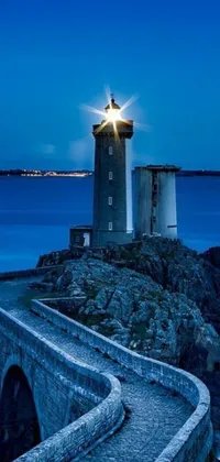 Enhance your phone wallpaper with our captivating blue night scene featuring a lighthouse standing tall on a rock next to the ocean