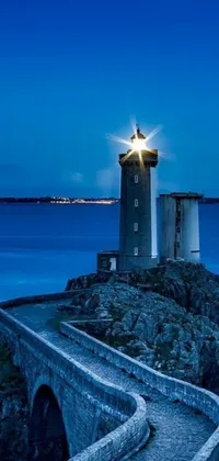 Immerse yourself in the peaceful and serene scene of a lighthouse, situated on a rocky outcrop next to the ocean, with this stunning live wallpaper