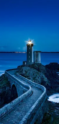 Looking for a mesmerizing live phone wallpaper? Your search ends here with this stunning blue lighthouse standing tall on rocky terrain by the ocean