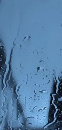 Transform your phone's screen with this stunning live wallpaper! Featuring a serene blue-grey background, this wallpaper showcases a close-up of raindrops cascading down a windowpane in a mesmerizing simulation