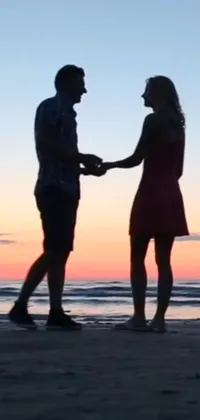 This live wallpaper for phones showcases a beautiful sunset on the beach with a couple holding hands