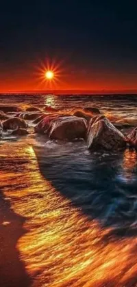This live phone wallpaper showcases an awe-inspiring sunset over a rocky shoreline, with a body of water nestled in the background