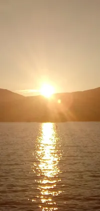 This stunning phone live wallpaper showcases a picturesque sunset over a serene body of water, with vibrant sunshine illuminating the lush mountain peaks in the distance
