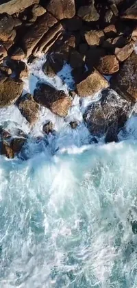 This phone live wallpaper features an aerial shot from a drone of a surfer riding a wave surrounded by big rocks