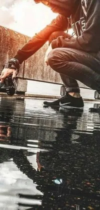 This live phone wallpaper features a hyper-realistic image of a man squatting next to a puddle, taking a photo with his phone