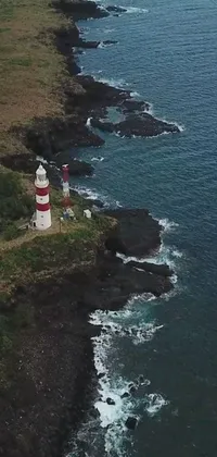 This live phone wallpaper features a picturesque lighthouse standing atop a rugged cliff alongside a magnificent ocean view