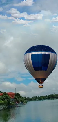 This lively live wallpaper showcases a mesmerizingly colorful hot air balloon, soaring over the calm waters