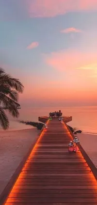 This phone wallpaper boasts a tropical-style wooden walkway that leads to an enchanting beach at sunset