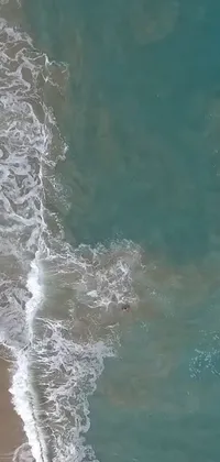 Enjoy a stunning phone live wallpaper of a surfer riding waves on a sandy beach