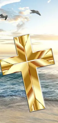This phone live wallpaper features a golden cross placed on a sandy beach