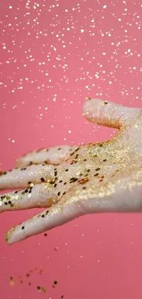 This phone live wallpaper features a close-up of a hand with gold paint, set against a background of lush sand and glitter